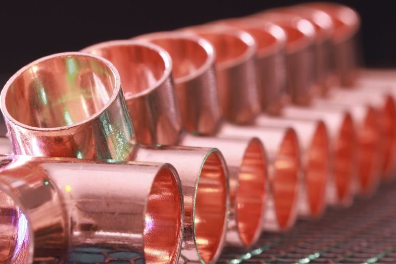 A row of copper tee fittings on a workbench, representative of supply-side work