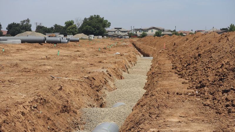 An open utility trench with bedding gravel and pipe, representative of underground line work
